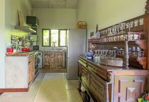 A kitchen with wooden cabinets, a refrigerator, and a window. - Green Cottage Chamarel (Chamarel)