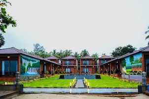 Una hilera de edificios tipo bungaló con una piscina central, rodeada de exuberante vegetación y palmeras.