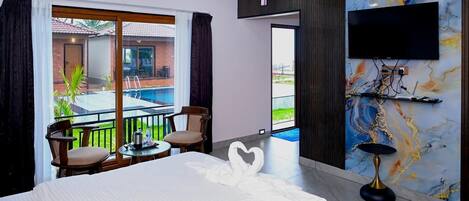Camera d'albergo con un letto grande, una TV montata su una parete in marmo, un balcone con piscina e vista su un edificio con tetto rosso.