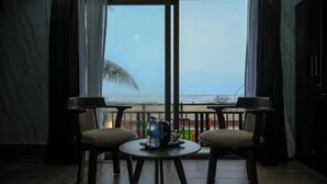Una habitación con dos sillas y una mesa, una ventana que da a la playa y una botella de agua sobre la mesa.