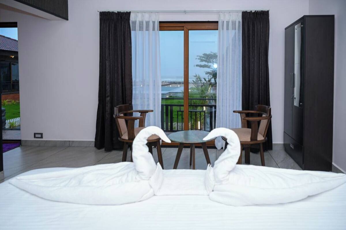A hotel room with a bed, two chairs, a table, and a view of the outdoors through a large window.