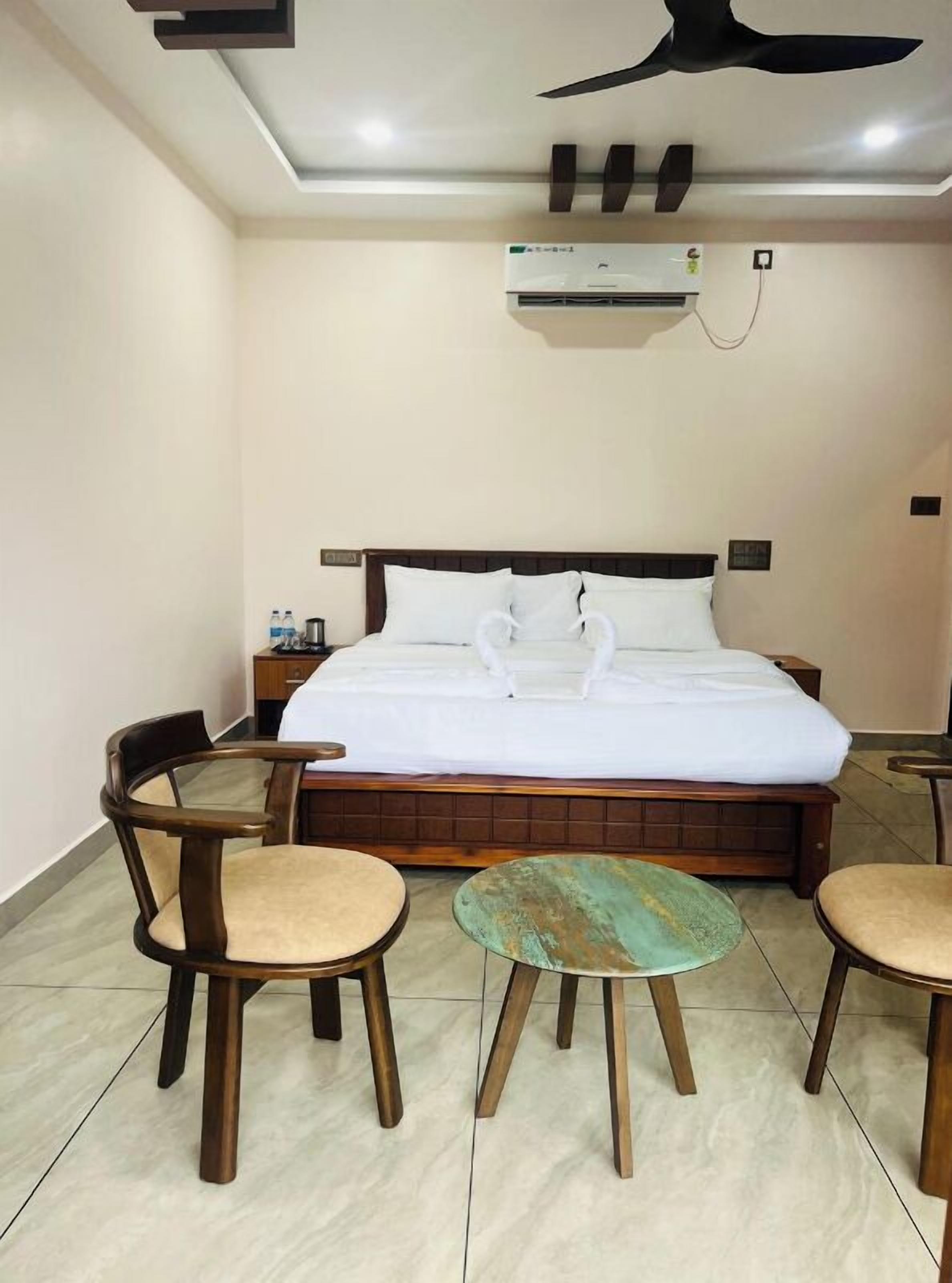 A hotel room with a bed, two wooden chairs, a small round table, and a ceiling fan.
