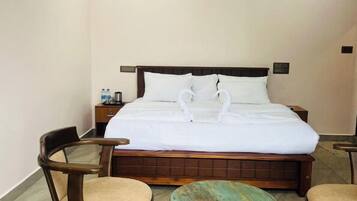 A hotel room with a bed, two wooden chairs, a small round table, and a ceiling fan.