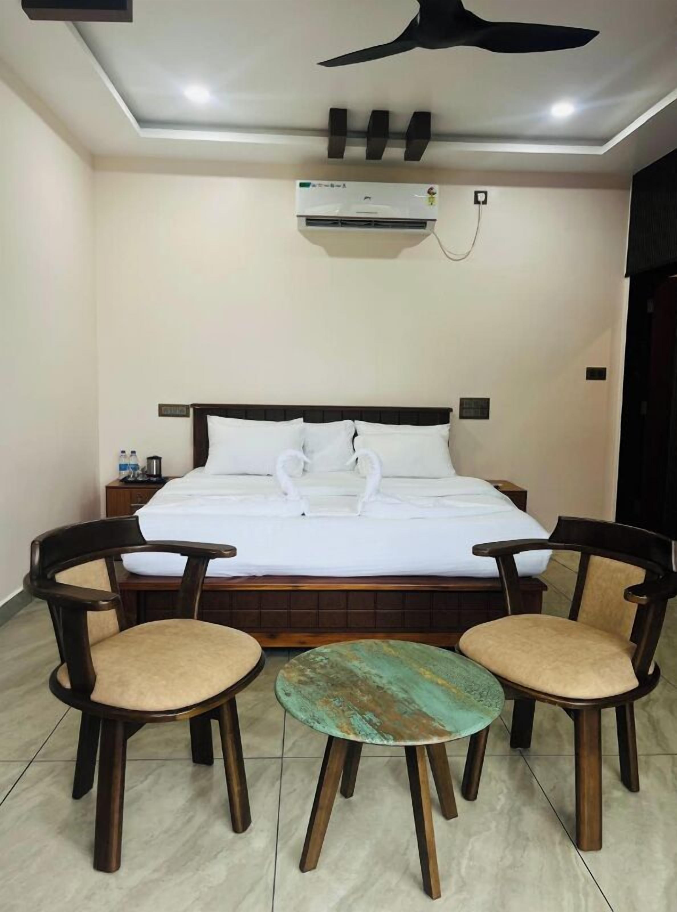 A hotel room with a bed, two chairs, a small table, a ceiling fan, and an air conditioning unit.