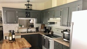A kitchen with grey cabinets, a wooden countertop, a stove, a microwave, and a coffee maker. - Peaceful Country Retreat (Webster)