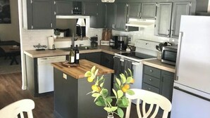 A modern kitchen with dark cabinets, a central island, and a dining area with a round table and chairs. - Peaceful Country Retreat (Webster)