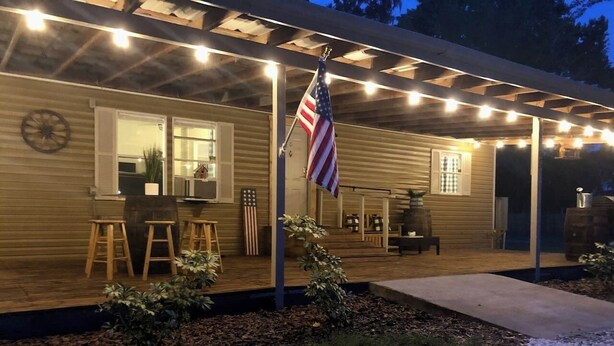 A wooden house with a covered porch, outdoor seating, and an American flag. - Peaceful Country Retreat (Webster)
