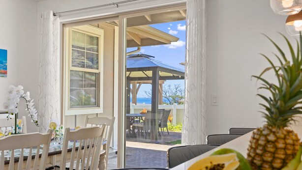 A dining area with a table and chairs, a large window with curtains, and a view of the outdoors. - @ML Ocean View, Golf, Gazebo and Bbq, we Have All! (Waianae)