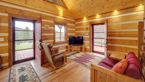 L’intérieur d’une cabane en rondins, avec un plancher en bois, un téléviseur posé sur un meuble, un fauteuil à bascule, un canapé et un tapis.