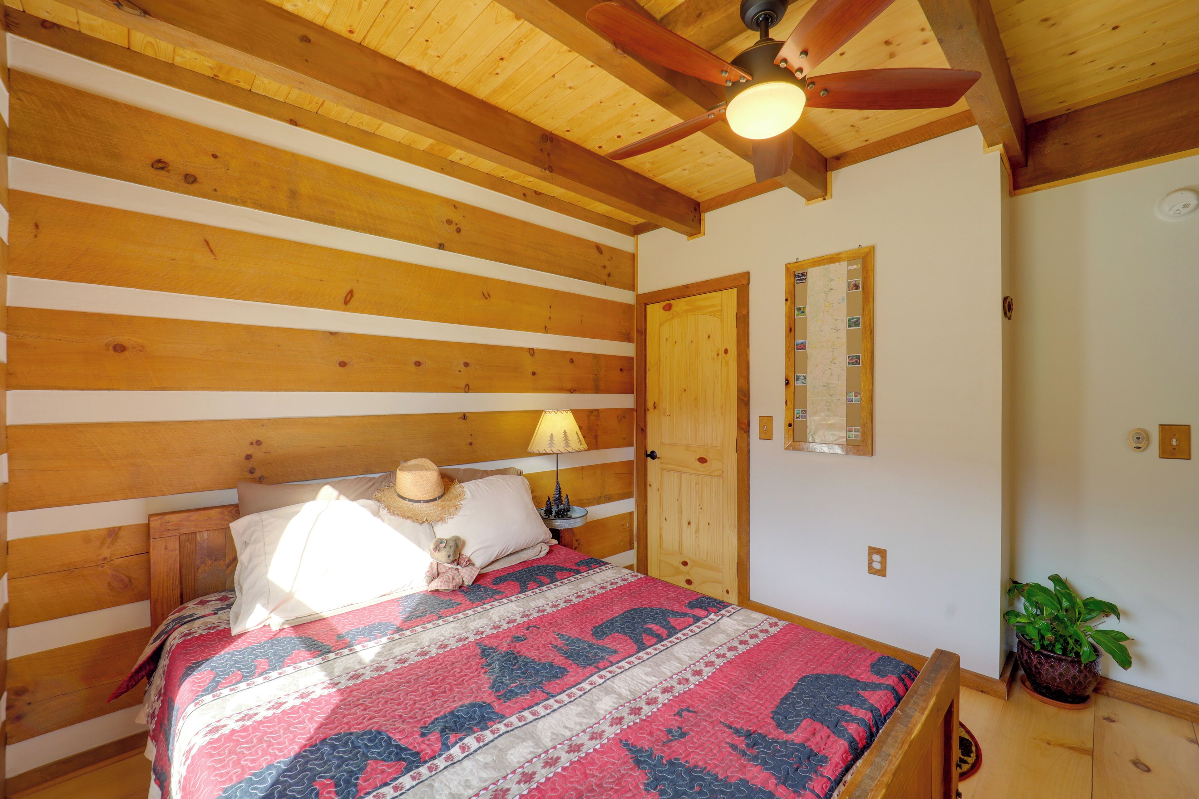 Een slaapkamer in een houten chalet met een bed, een nachtkastje, een lamp en een plafondventilator.