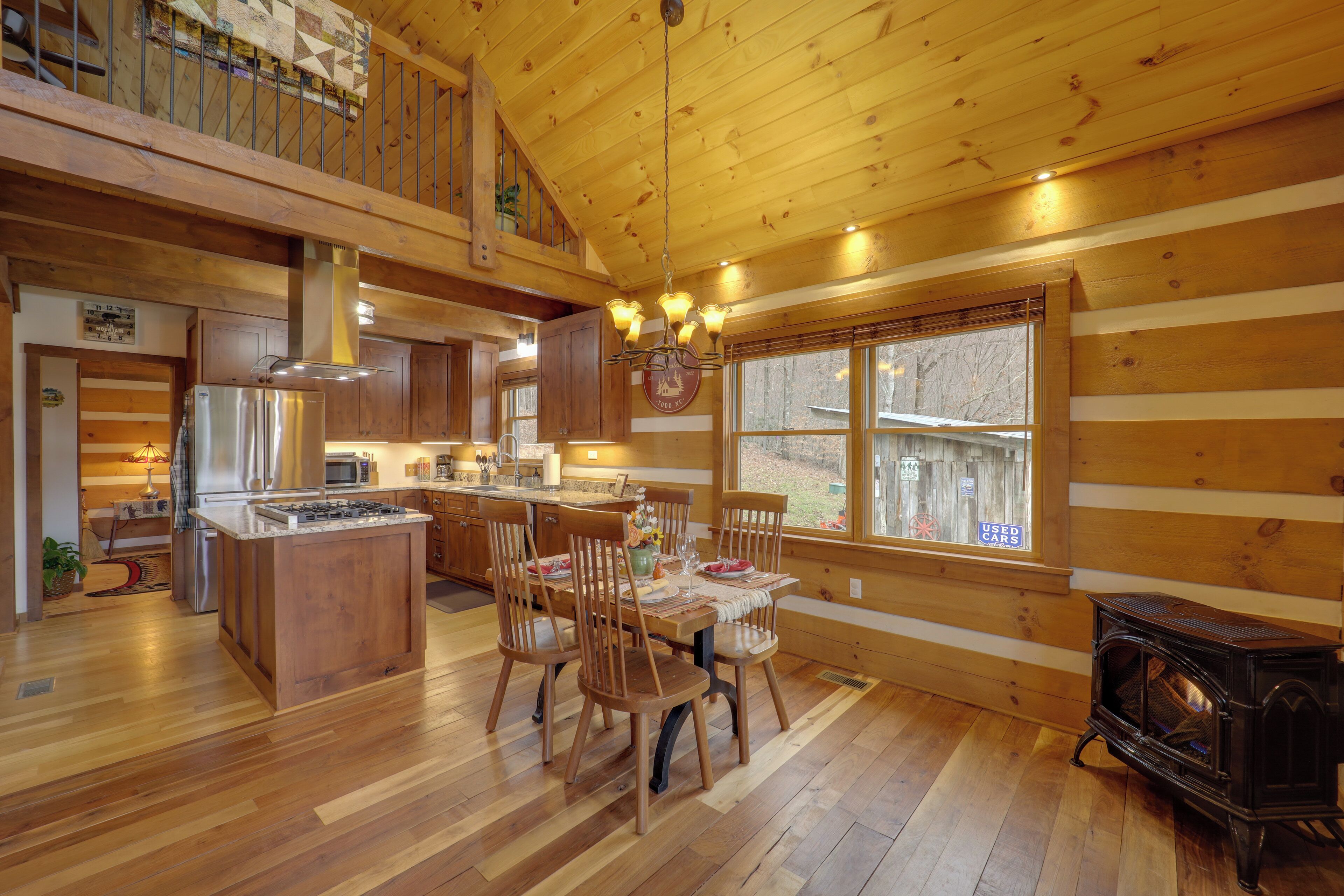 Interior de una cabaña de madera con comedor, cocina y estufa de leña.