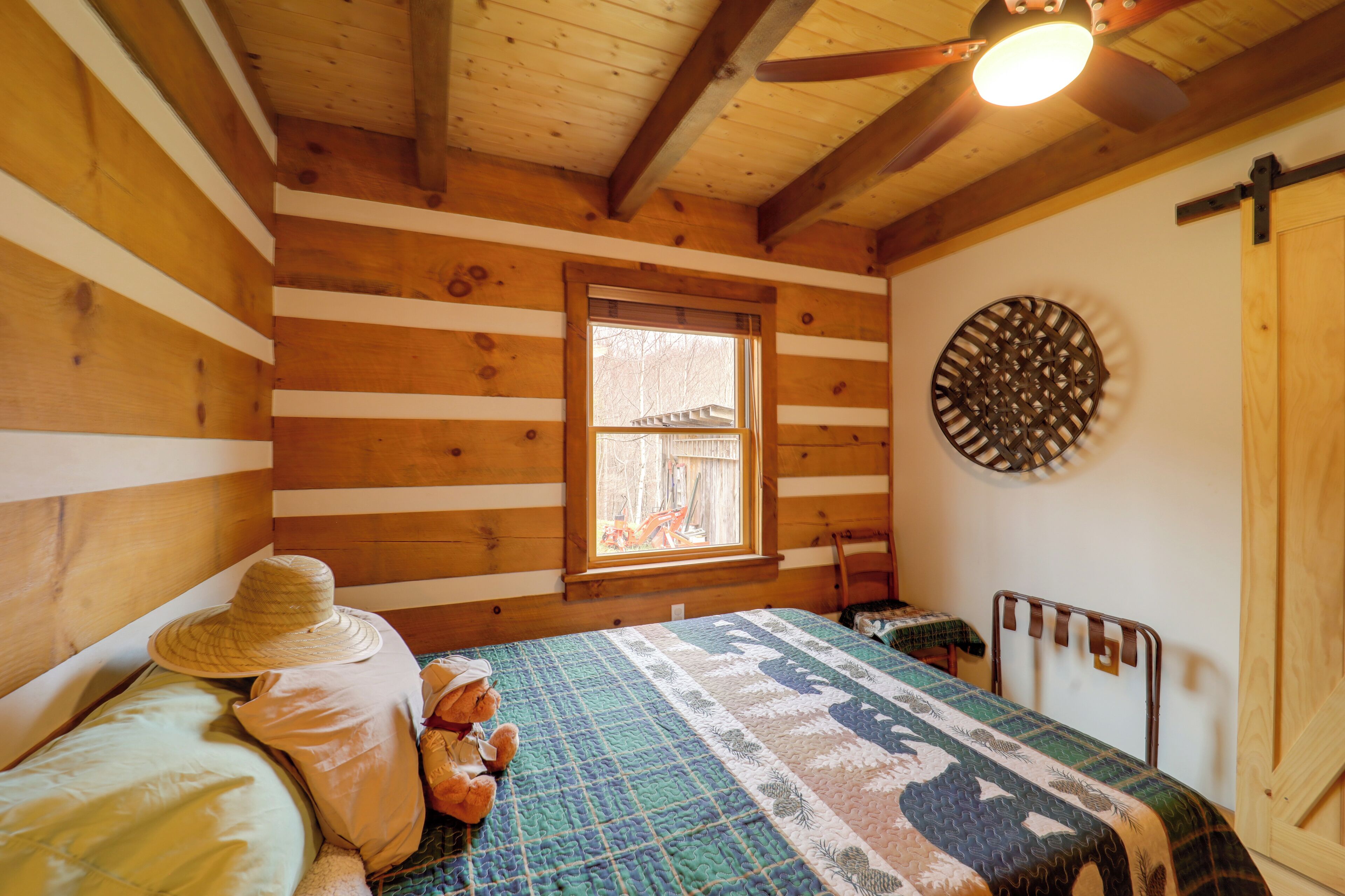 A cozy log cabin room with a bed, a window, a circular wall decoration, and a wooden door.