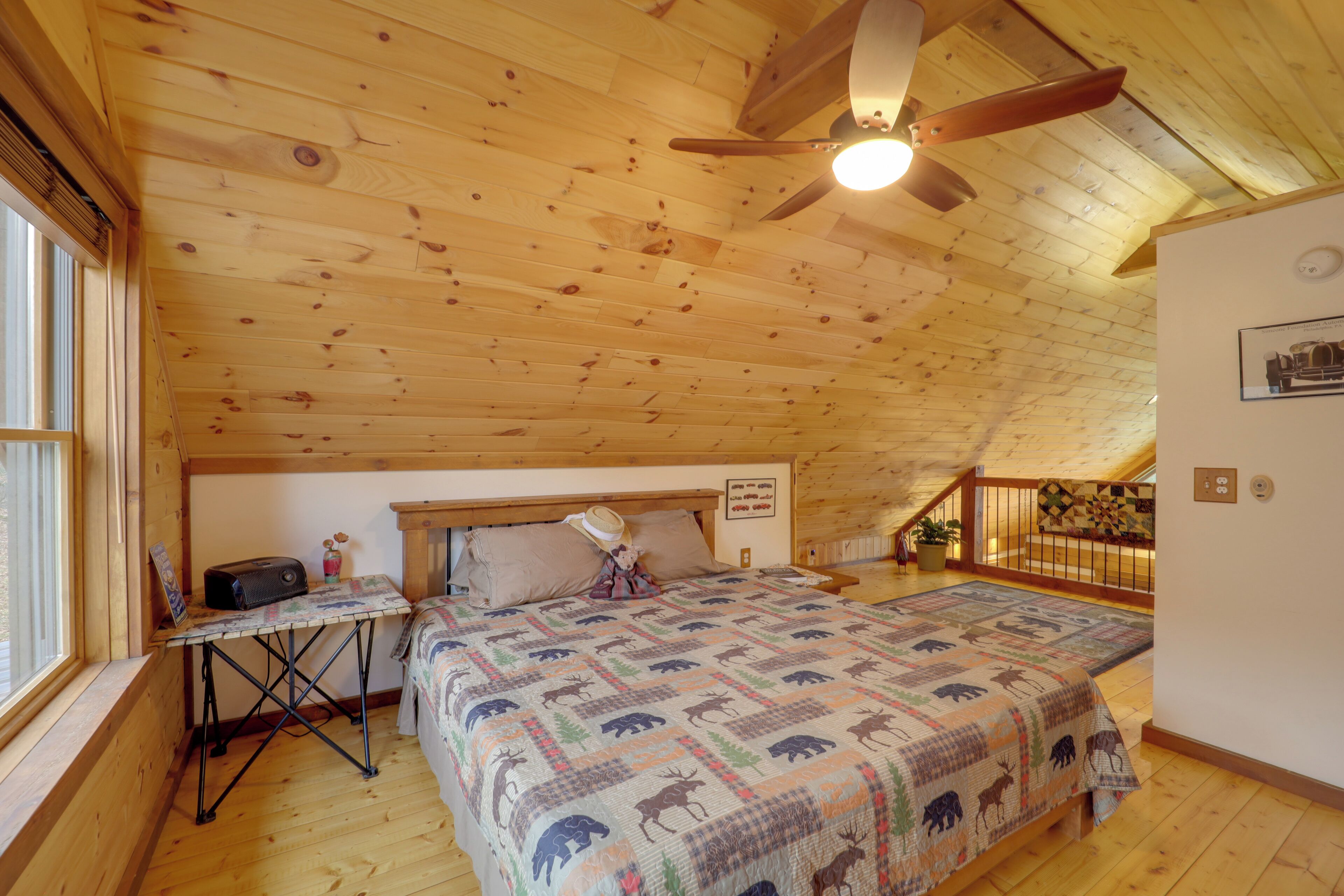 Un dormitorio con techo de madera, una cama con colcha estampada, un escritorio con radio y una ventana con persianas.