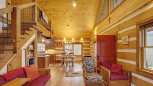 L’intérieur d’une cabane avec un escalier en bois, un coin repas, un canapé, un fauteuil et une porte rouge.