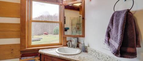 A wooden cabin bathroom with a large window, a white sink, wooden cabinets, and a towel rack.