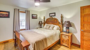 Een slaapkamer met een houten bed, bedlampen, een nachtkastje, een houten bankje en een plafondventilator.