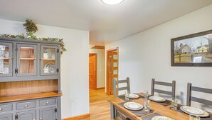 Een eetruimte met een houten tafel voor vier personen, een grijs kastje met glazen deuren, en een lijst met een afbeelding aan de muur.