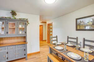 Un comedor con una mesa de madera dispuesta para cuatro personas, un mueble gris con puertas de vidrio y un cuadro en la pared.
