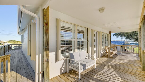 A wooden deck with a white sofa and a bench, large windows, and a view of the ocean.