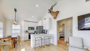 A modern kitchen with white cabinets, a central island with bar stools, a mounted animal head, and a dining area with wooden furniture.