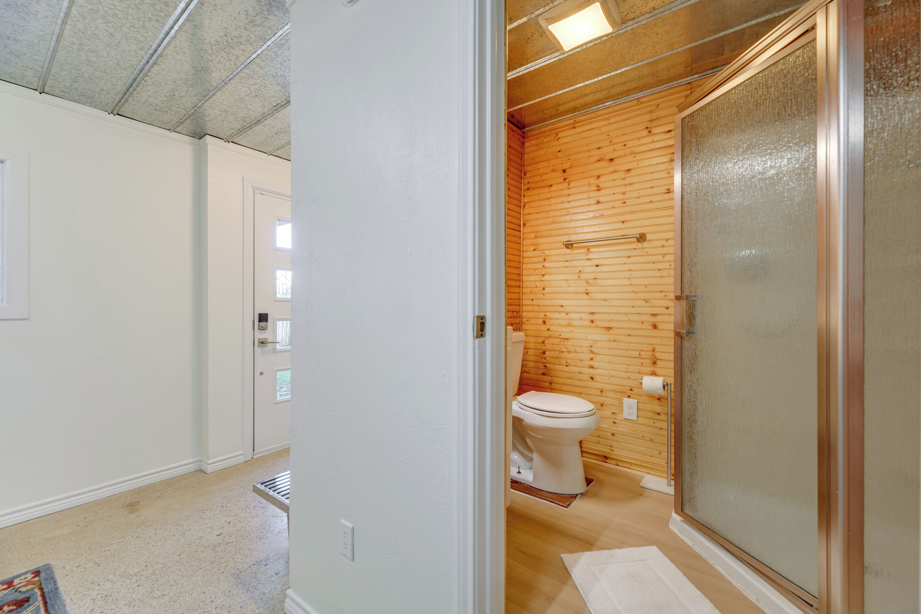 Ein Badezimmer mit einer Holzwand, einer weißen Toilette und einer Duschkabine aus Glas.