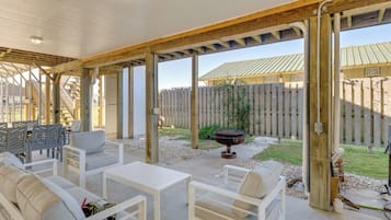 An outdoor patio with white furniture, a barbecue grill, and a wooden pergola structure.