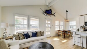 A spacious living area with a white sofa, a dining table, and a kitchen area with white cabinets and a hanging light fixture.