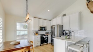 A modern kitchen with white cabinetry, a central island with bar stools, a built-in oven, and a stainless steel refrigerator.