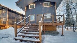 A wooden staircase leading to a wooden deck with a metal railing, surrounded by snow.