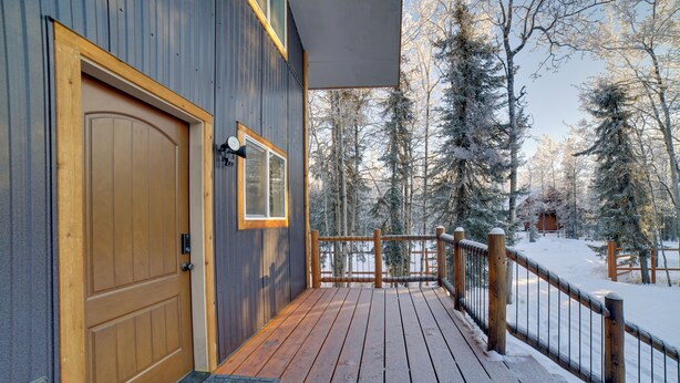 A wooden deck with a wooden door and a window, surrounded by snow-covered trees.