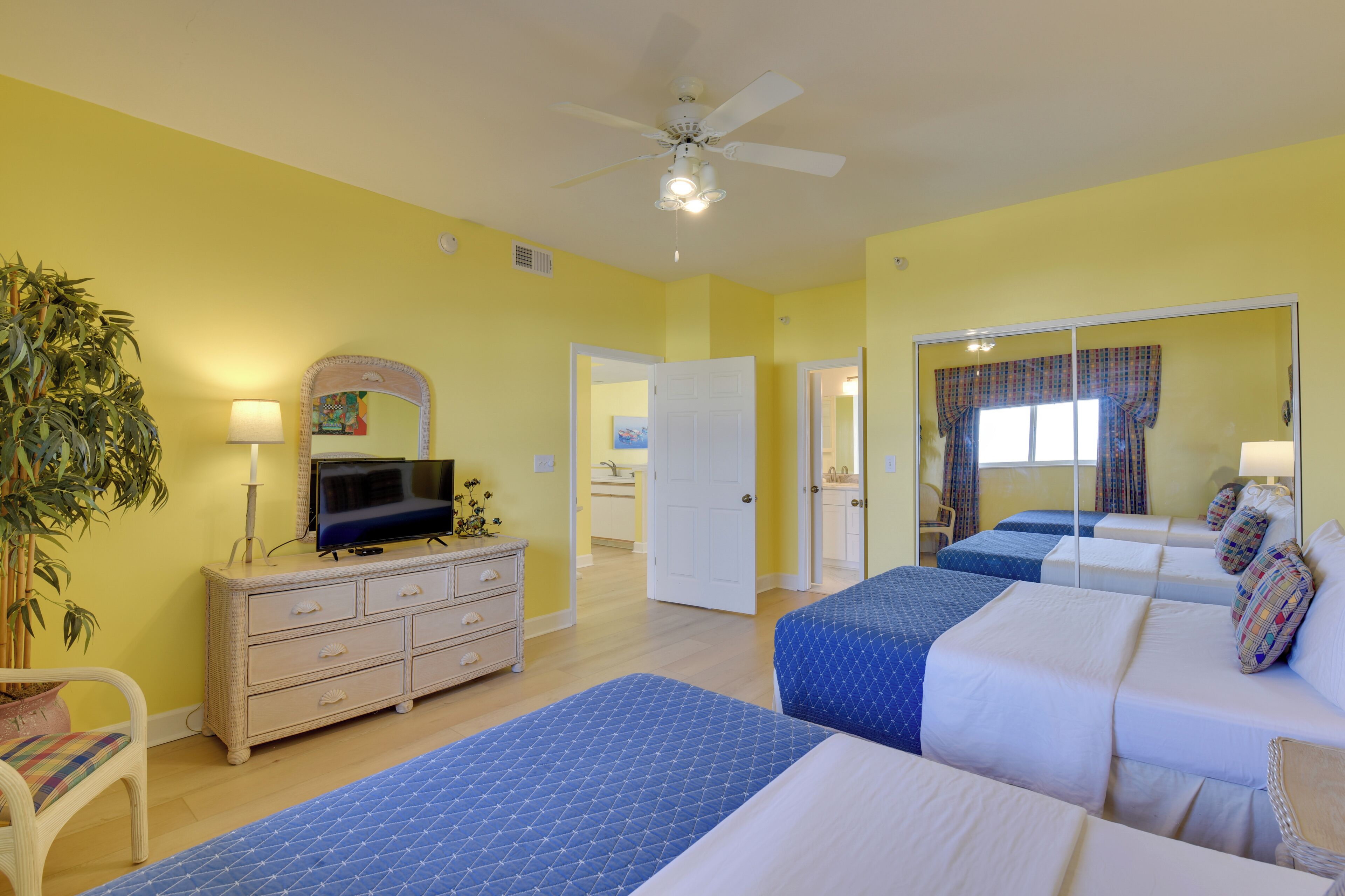 A hotel room with two beds, a TV, a dresser, and a ceiling fan.