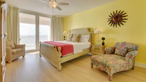 A bedroom with a bed, two chairs, a nightstand, a ceiling fan, and a sun decoration on the wall. - Navarre Condo w/ Beach Access & Ocean Views! (Navarre)