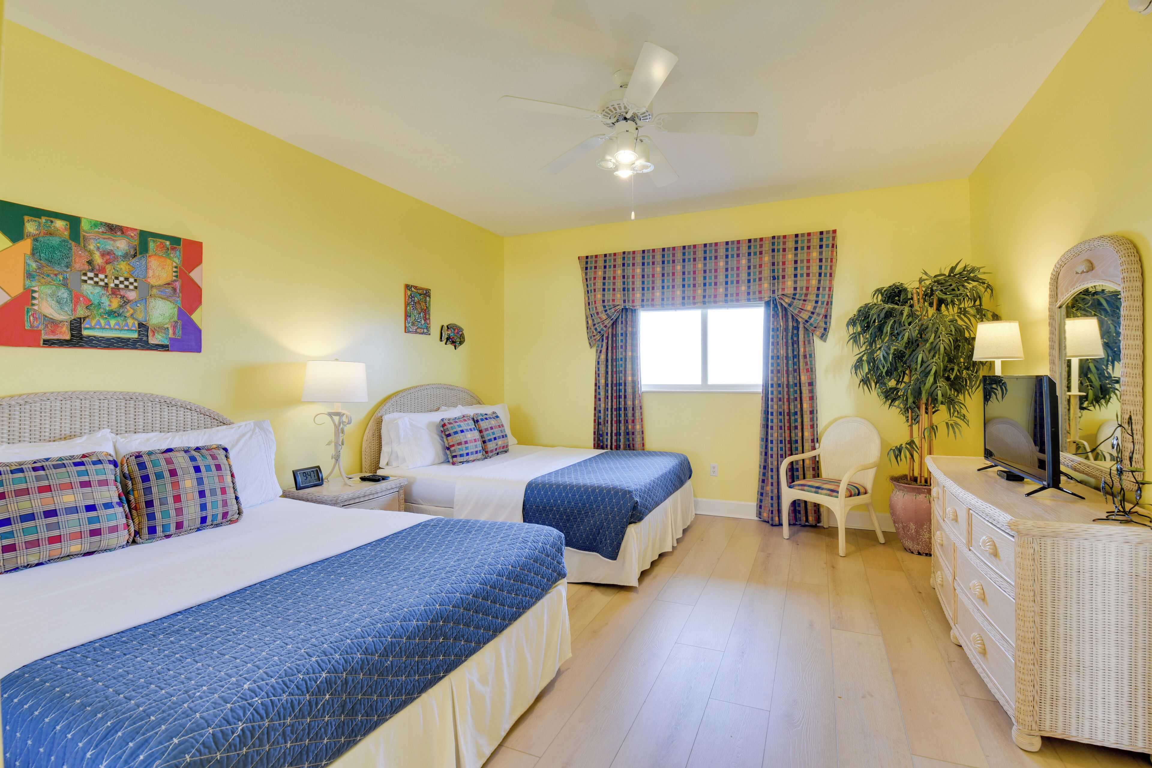 A hotel room with two beds, a ceiling fan, a TV, a dresser, a chair, and a window with curtains.