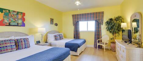 A hotel room with two beds, a ceiling fan, a TV, a dresser, a chair, and a window with curtains.