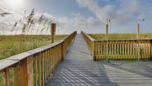 A wooden boardwalk leading through a grassy field with tall grasses and a clear sky. - Navarre Condo w/ Beach Access & Ocean Views! (Navarre)
