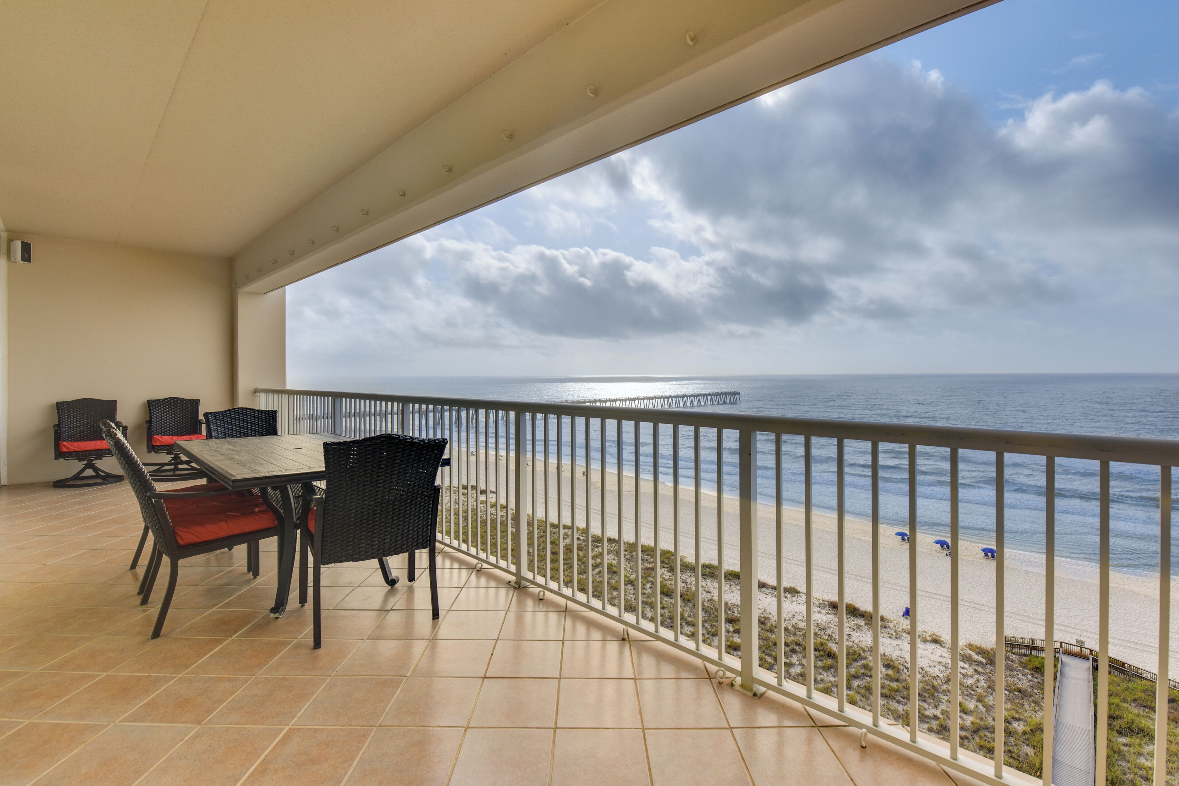 Un balcón con mesa y sillas, con vistas a una playa y una barandilla, y una vista despejada del océano.