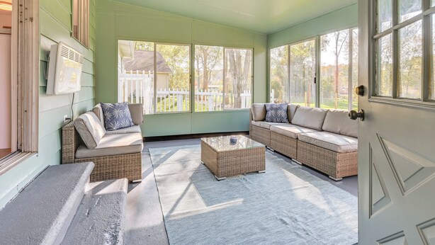 A sunroom with wicker furniture, large windows, and a view of a white picket fence. - Sand Lake Retreat: Canal Access & Large Yard! (Onsted)