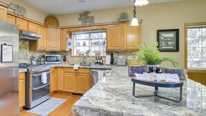 A kitchen with wooden cabinets, a granite countertop, a refrigerator, a stove, and a window with a view of trees.