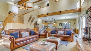 A spacious living room with leather sofas, wooden beams, and a fireplace.