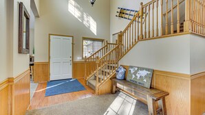 A spacious foyer with a wooden staircase, a bench, and a rug.