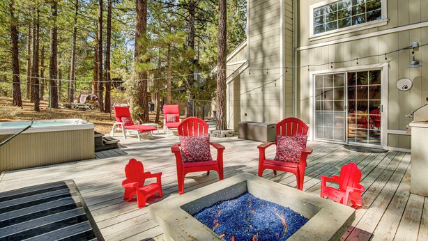 A deck with red Adirondack chairs, a hot tub, and a fire pit.