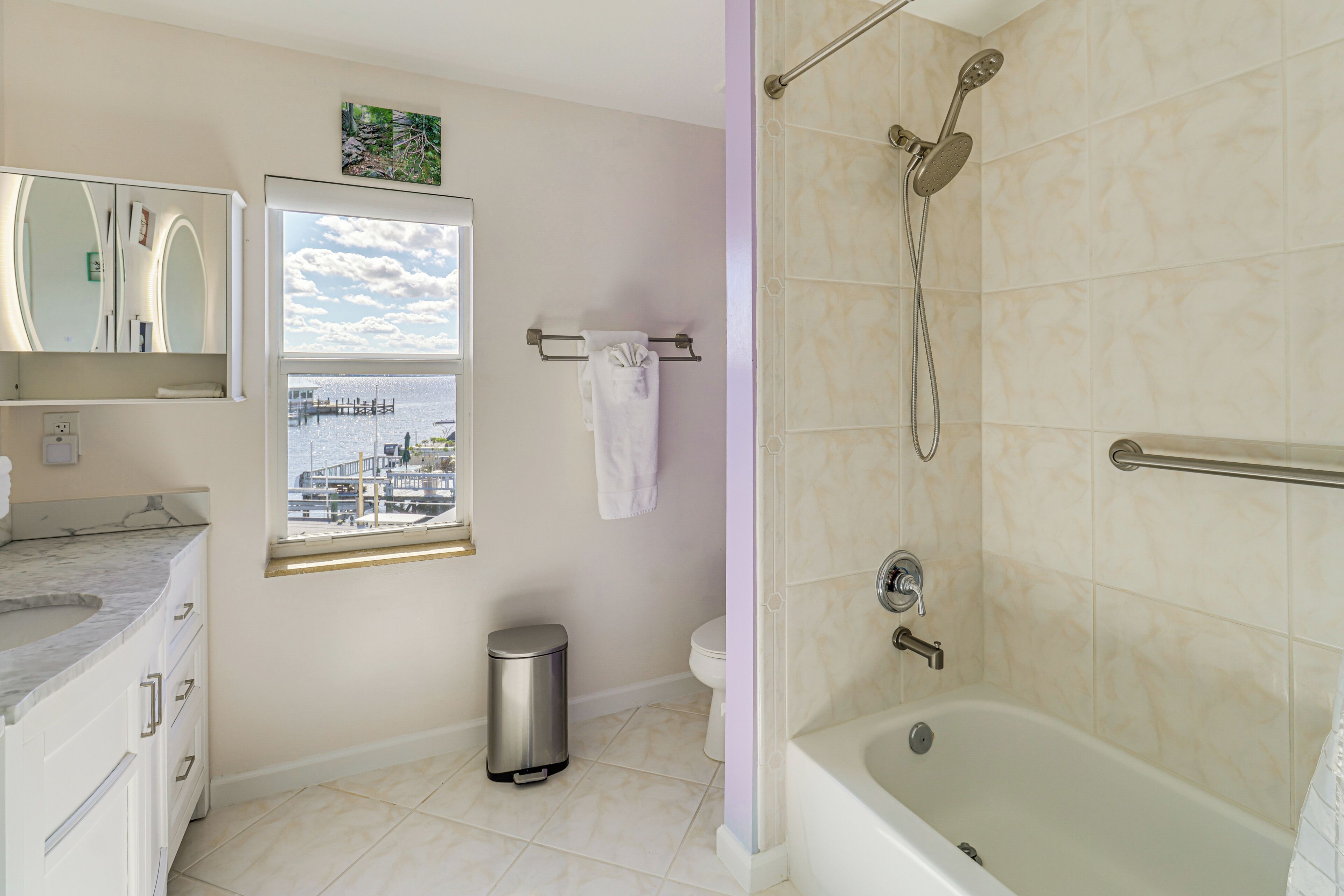 Ein Badezimmer mit einer Badewanne, einem Fenster mit Blick auf einen Steg, einer Toilette und einem Mülleimer.