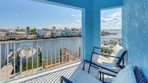 Un balcon donnant sur un port de plaisance, un ventilateur de plafond et un coin salon avec des coussins.