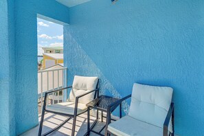 Ein Balkon mit zwei weißen Sitzgelegenheiten und einem kleinen Tisch, mit Blick auf ein Gebäude mit einem grünen Dach.