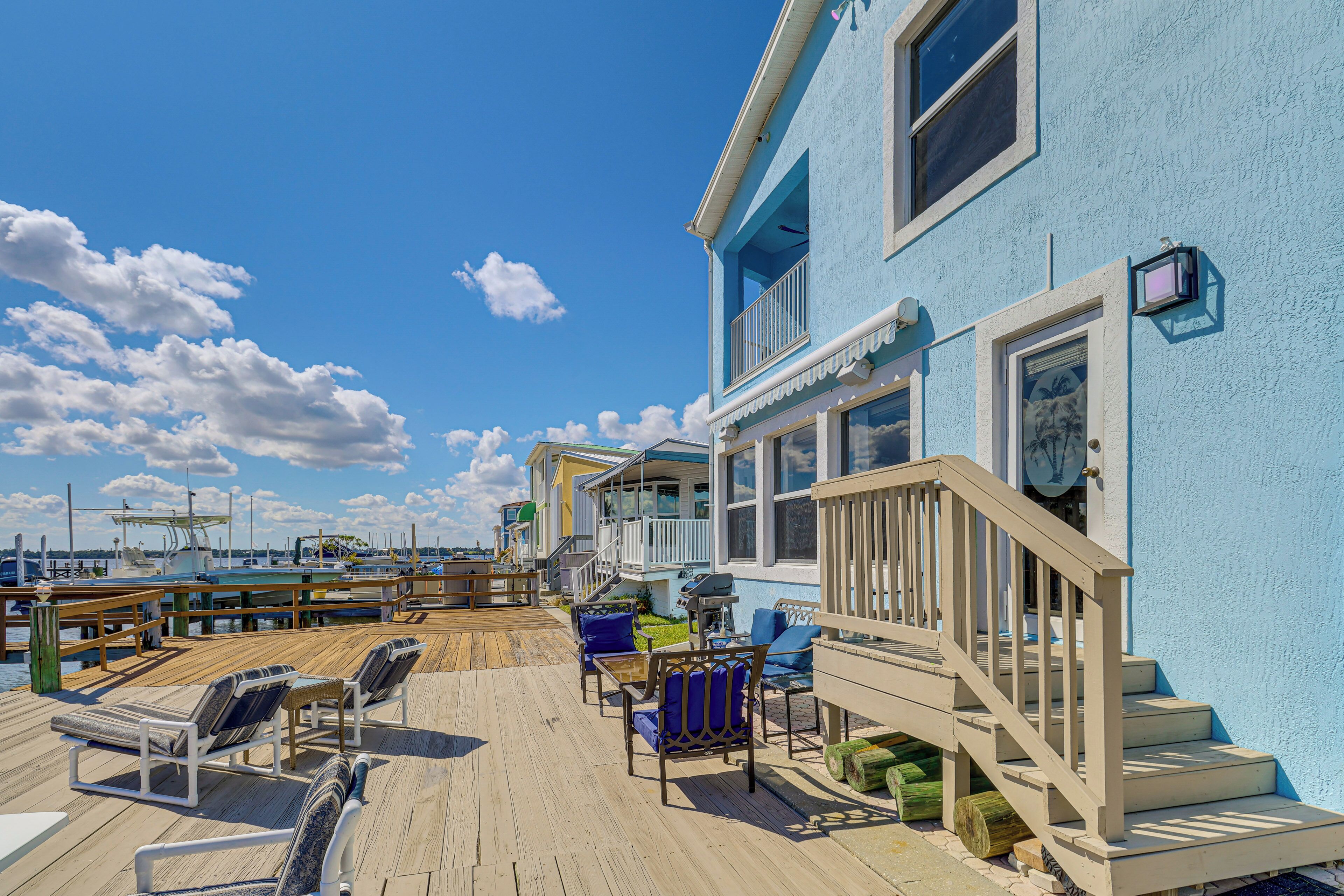 Eine Holzterrasse mit Sitzgelegenheiten im Freien, eine Treppe zu einem Balkon und im Hintergrund der Blick auf den Hafen.