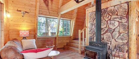 L’intérieur chaleureux d’un chalet avec un plafond en bois, une cheminée en pierre, un canapé agrémenté de coussins et une petite table.