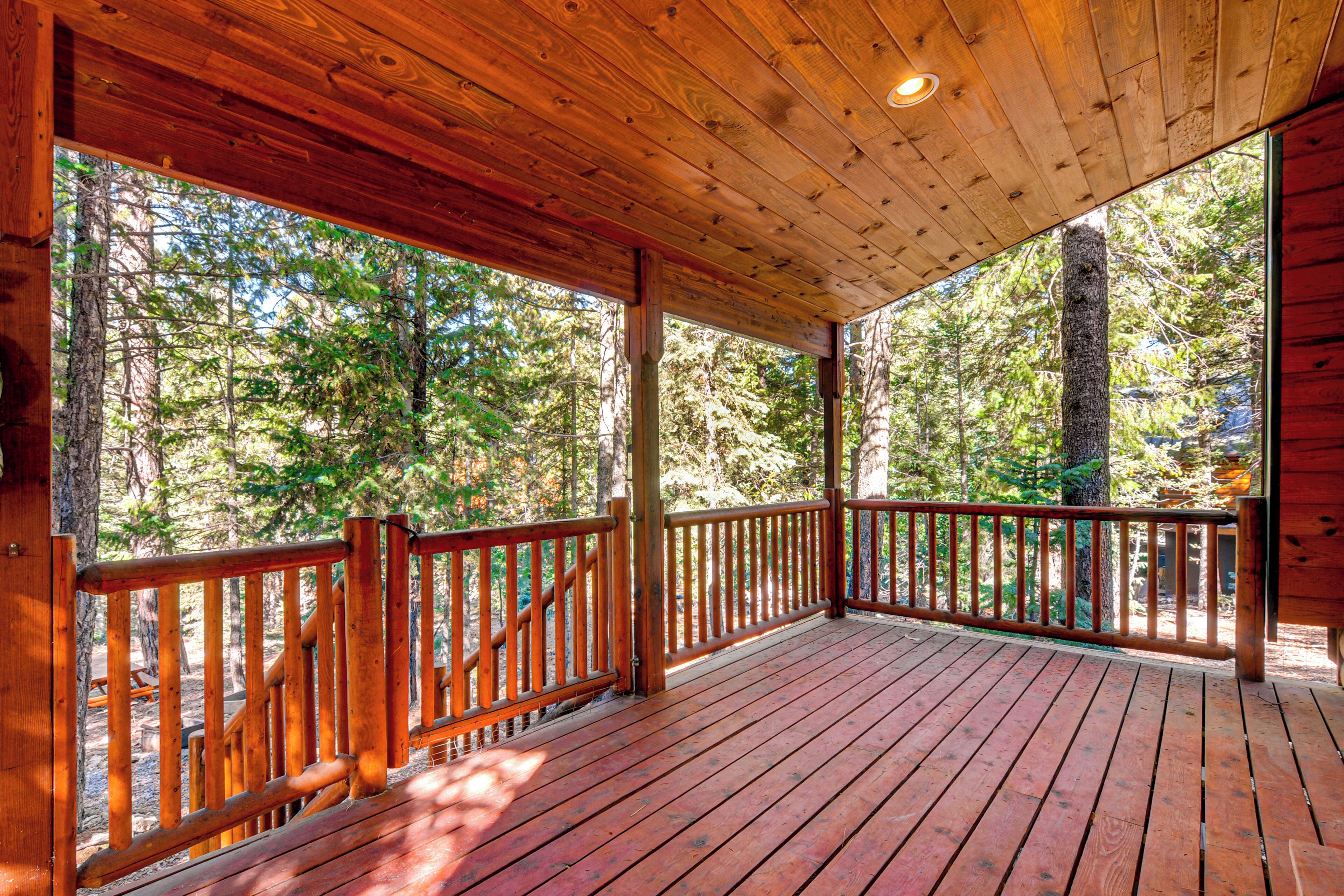 A wooden deck with a railing, surrounded by trees.