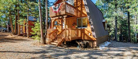 A wooden cabin with a balcony, surrounded by trees and gravel.