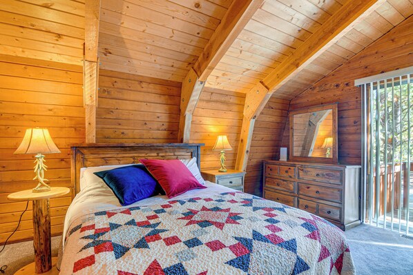 Un dormitorio de cabaña de madera con cama, mesitas de noche, cómoda y un ventanal grande.