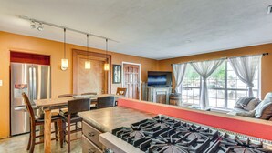 Una cocina con estufa a gas, sillas de madera, una mesa de comedor y un televisor al fondo.